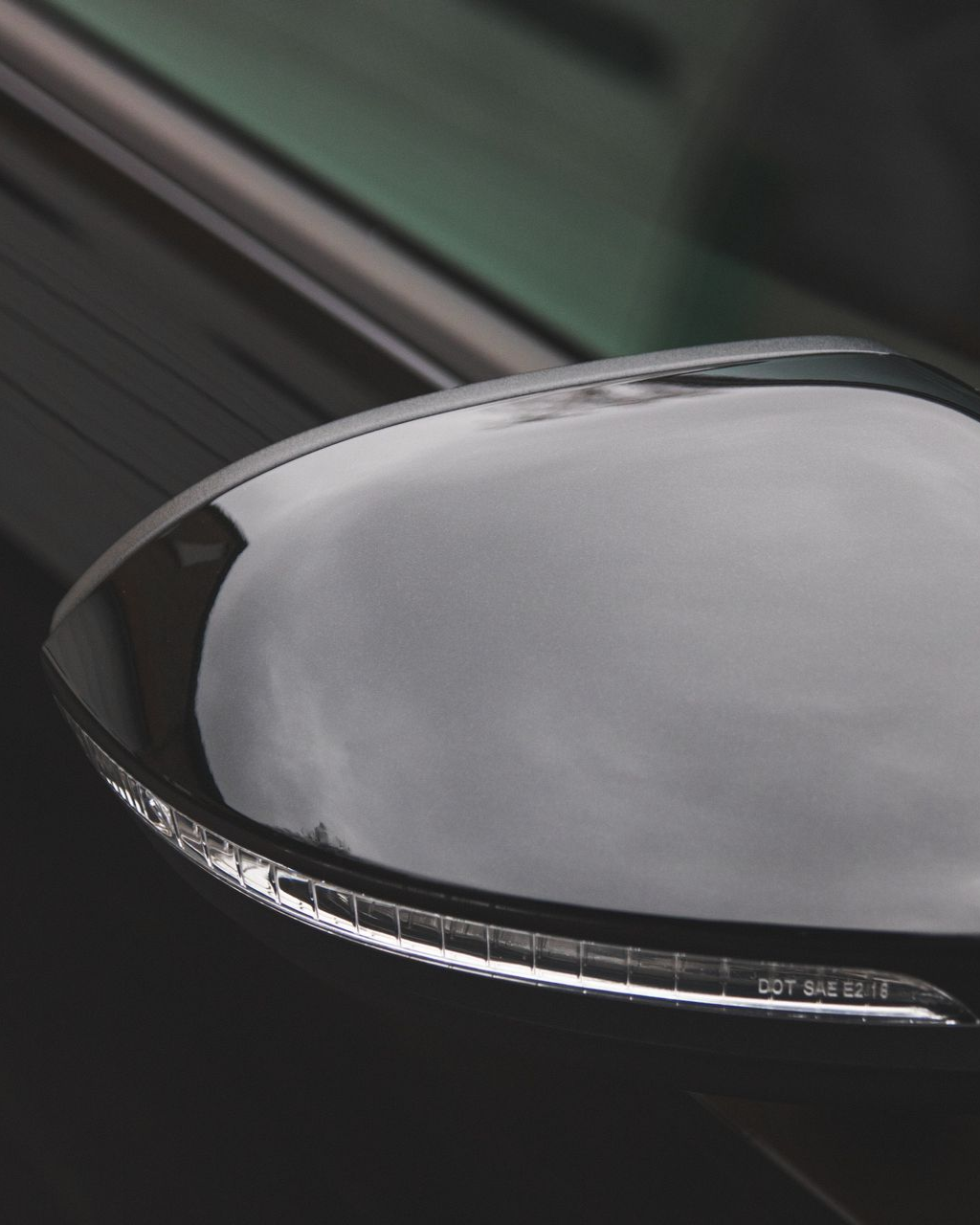 Close-up of a car side mirror with a glossy black housing and reflective glass