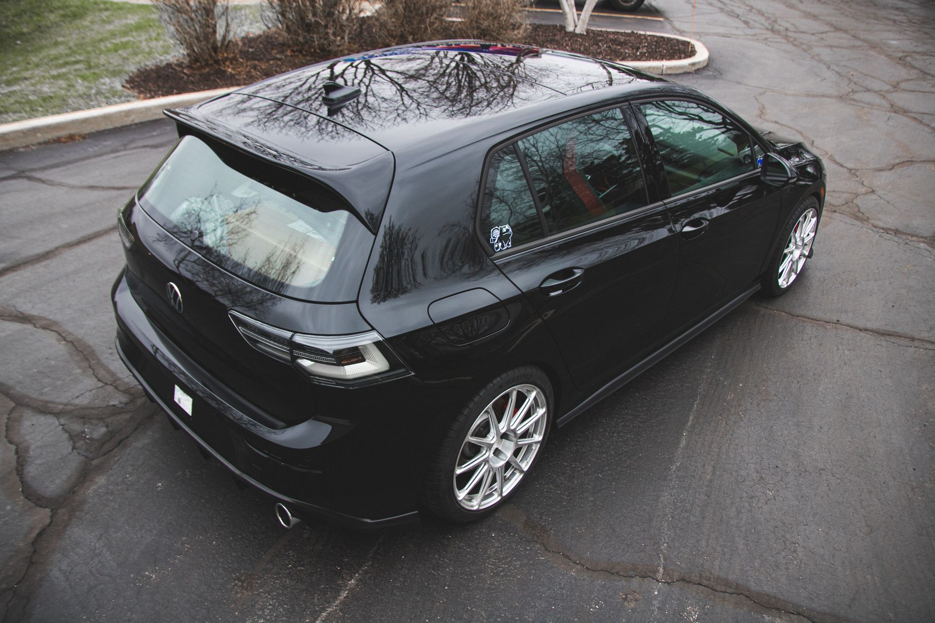Black hatchback parked on wet pavement near a curb, viewed from above.