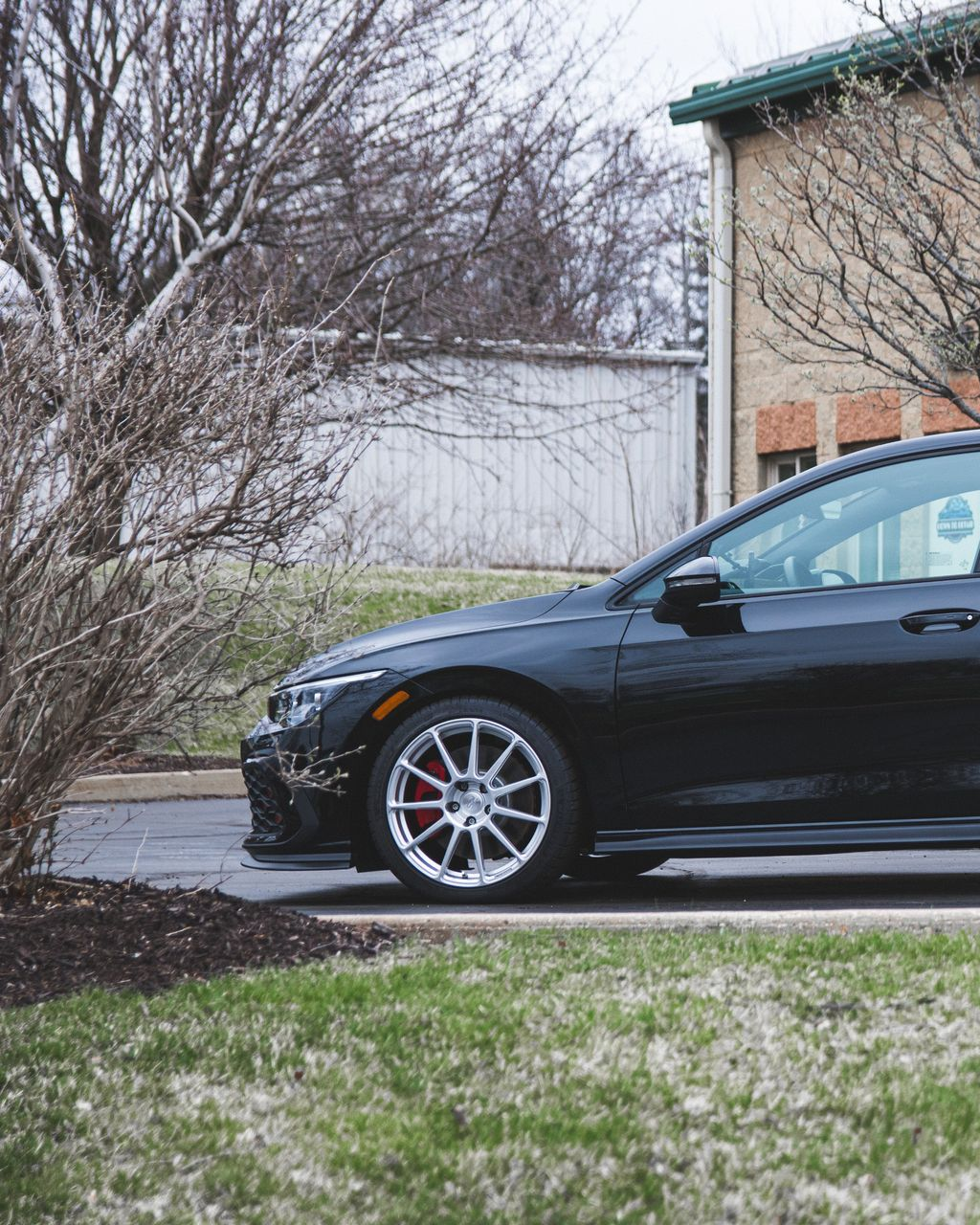 Black sedan parked by a house and leafless tree in a suburban yard