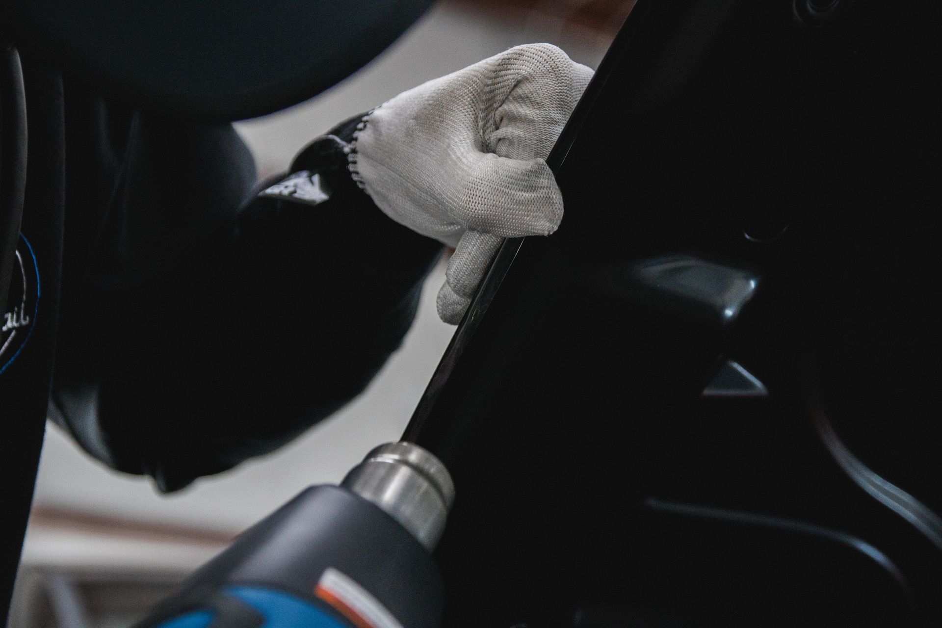 Gloved hand holding a car part while a power tool works nearby