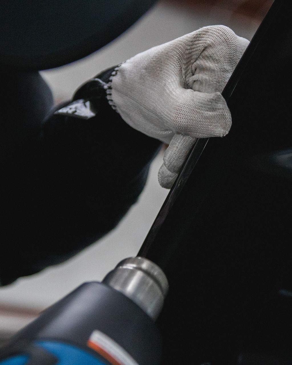 Gloved hand using a power screwdriver on a dark vehicle panel