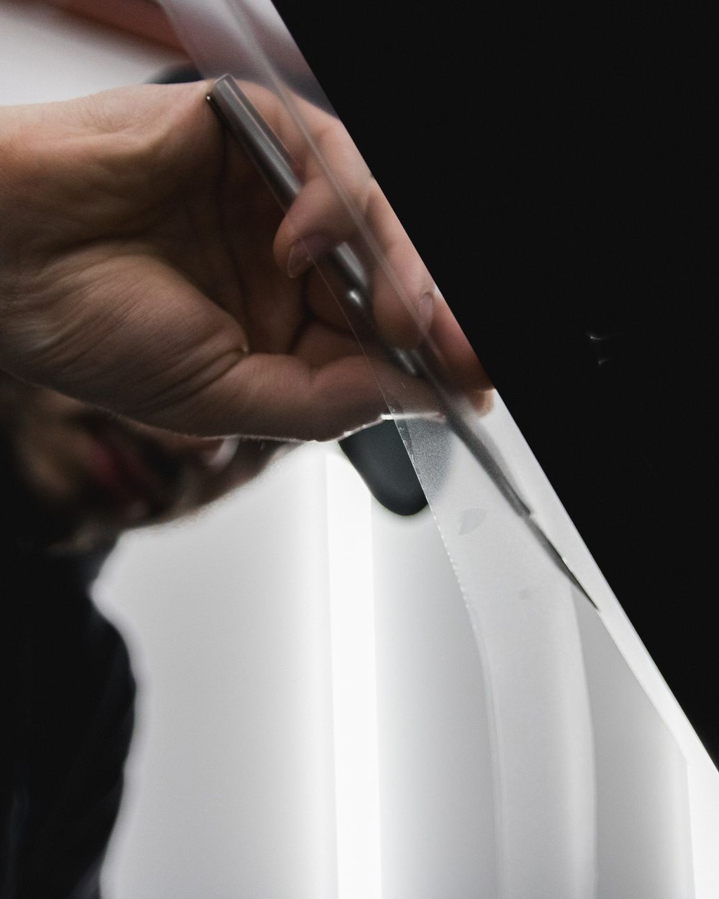 Hand using a pen to draw on a white surface, with a dark background