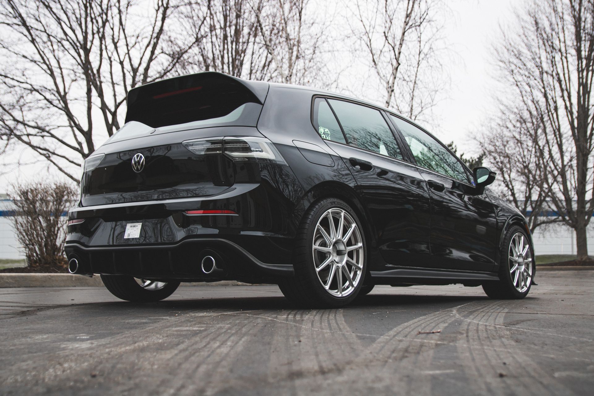 Black hatchback car parked on a wet road, rear view with bare trees in the background