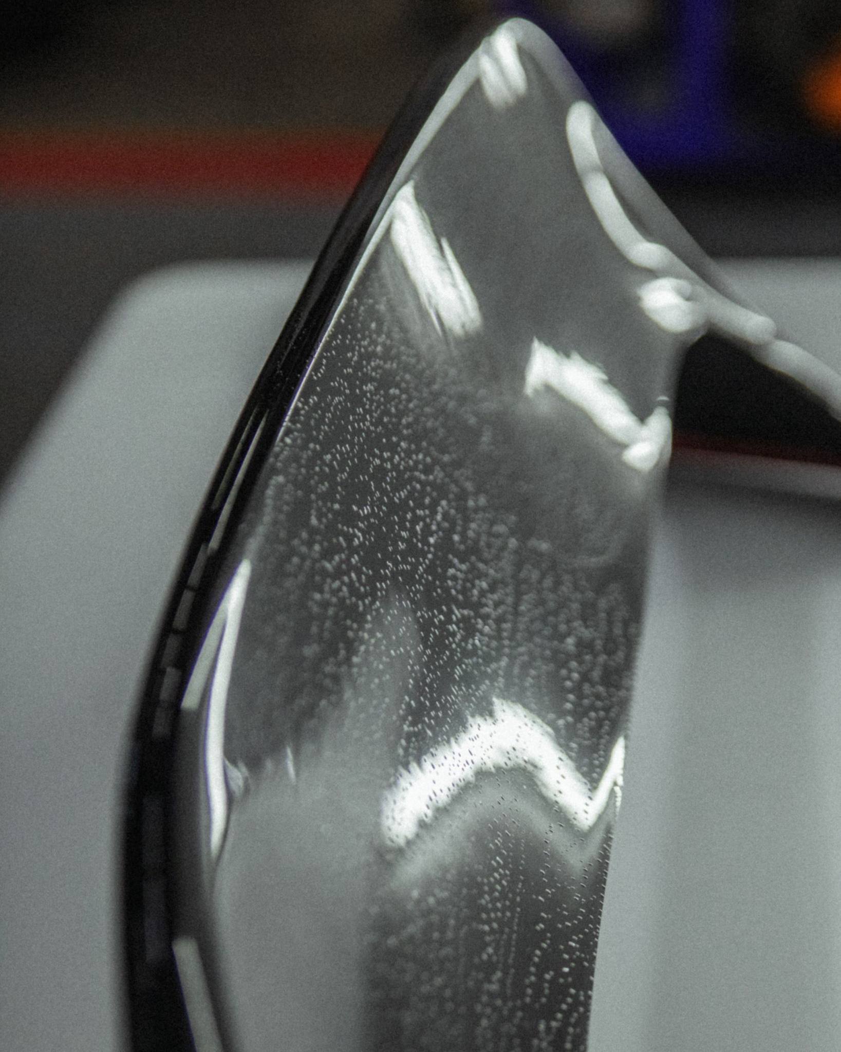 Close-up of a glossy black curved surface with bright reflections against a blurred gray background