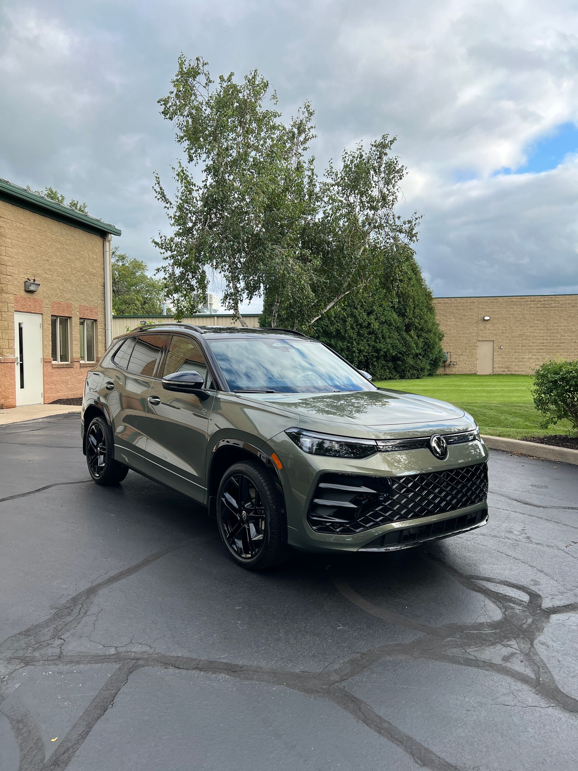 Gray SUV parked on a wet driveway beside a house under cloudy skies