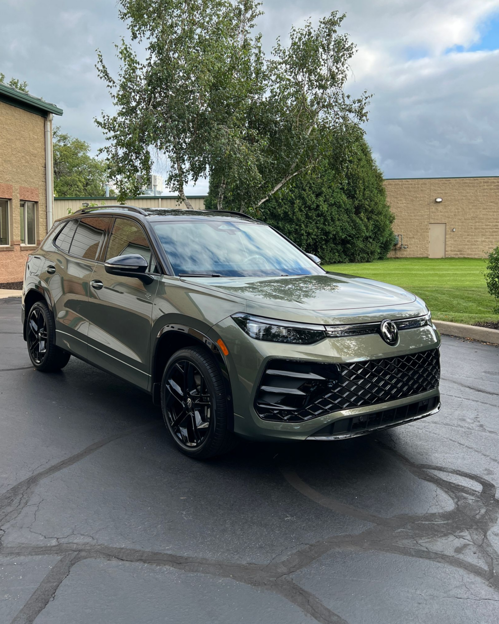Dark green Volkswagen SUV parked on a wet driveway near a brick building and grassy lawn