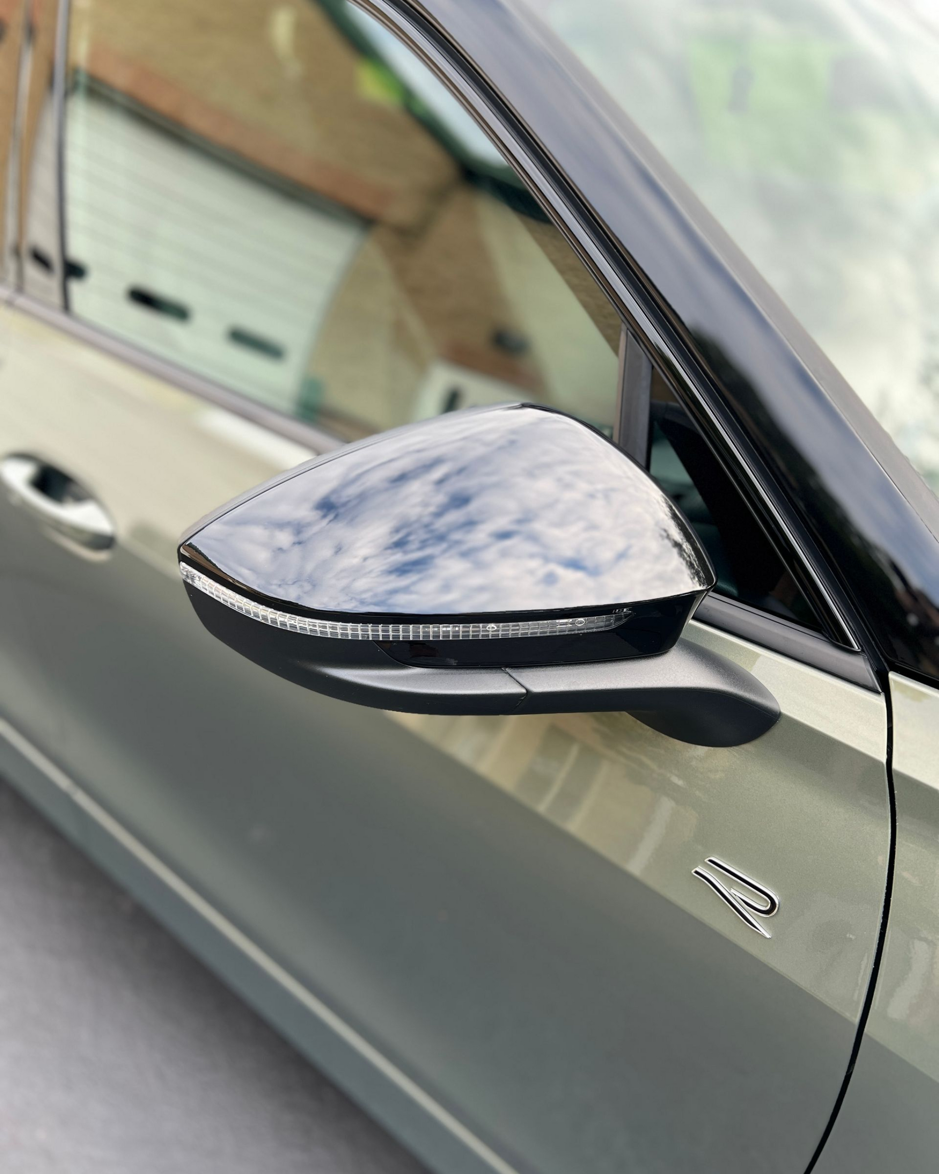 Close-up of a car’s side mirror on a gray vehicle, with a blurred garage in the background