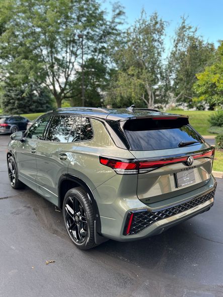 Green SUV parked on a tree-lined street, rear three-quarter view