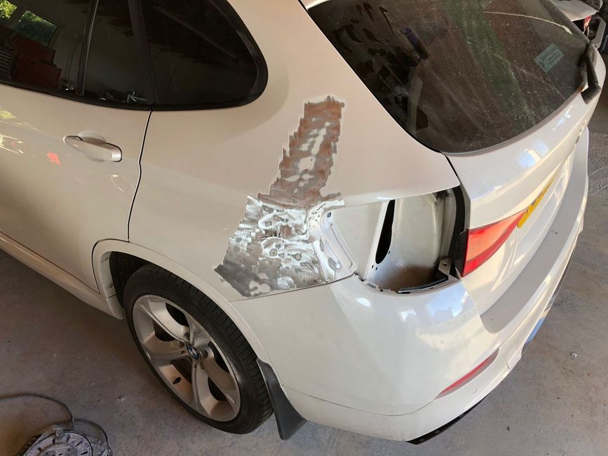 a white car with a damaged fender is sitting in a garage