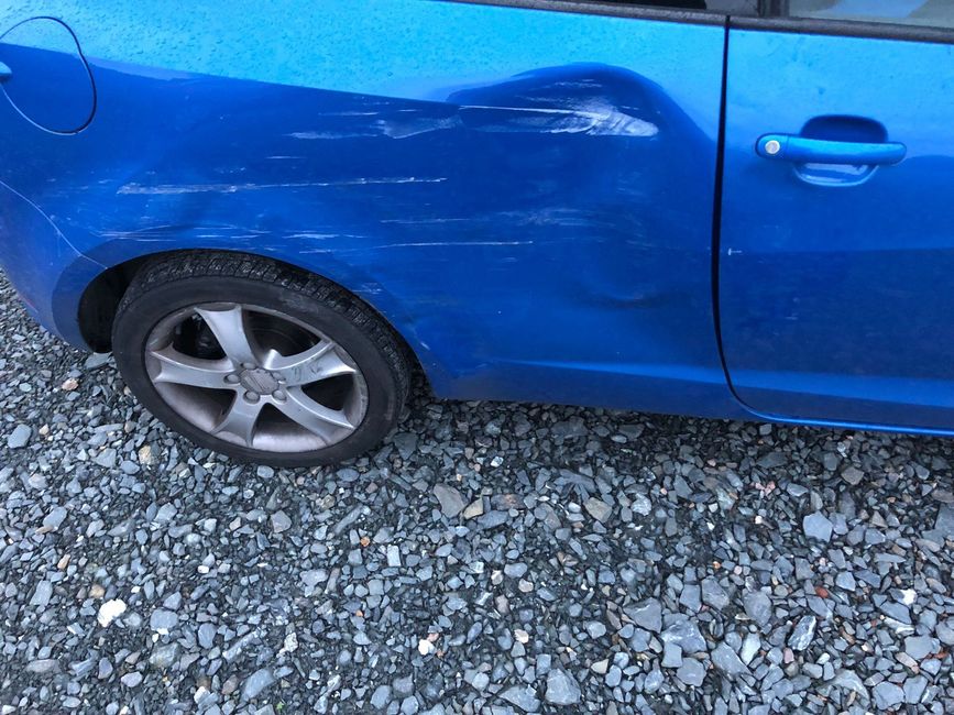 a blue car with a damaged side is parked on gravel