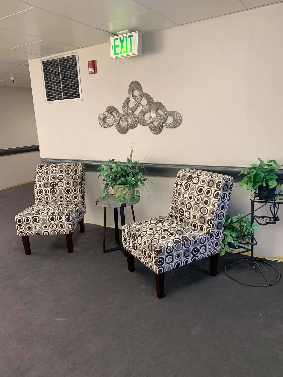 Two chairs and a table in a hallway with a green exit sign.