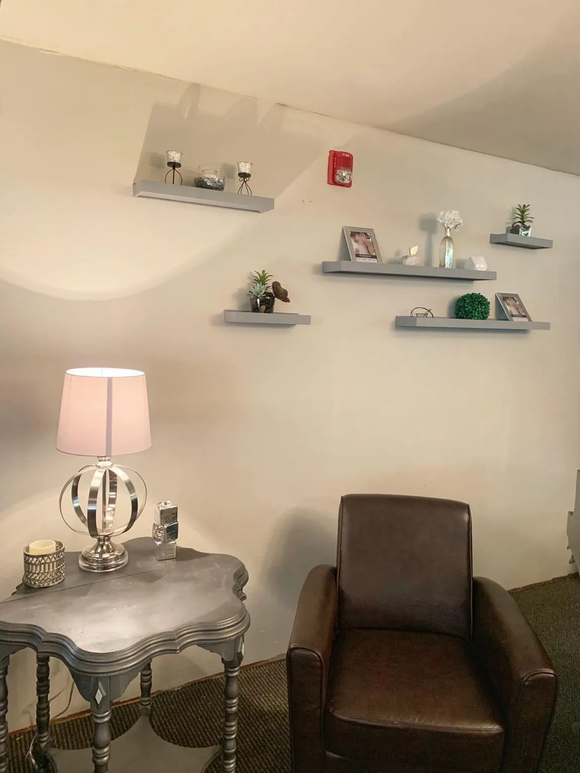 A living room with a chair , table , lamp and shelves.