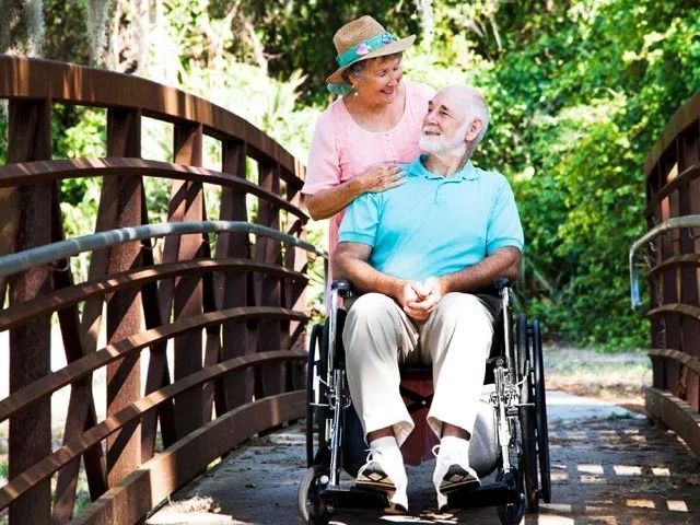 A man in a wheelchair is being pushed across a bridge by a woman
