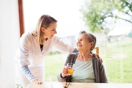A nurse is giving an elderly woman a glass of orange juice.