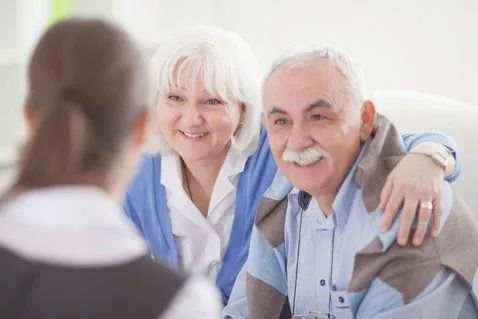 An elderly couple is sitting on a couch talking to a doctor.