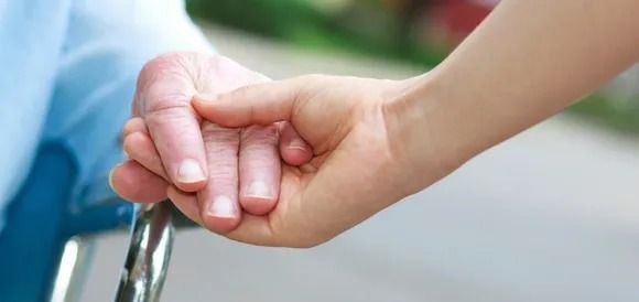 A woman is holding the hand of an elderly man in a wheelchair.