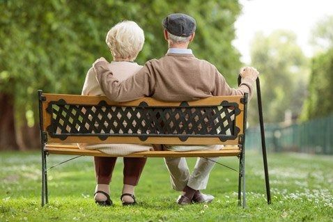 An elderly couple is sitting on a park bench.