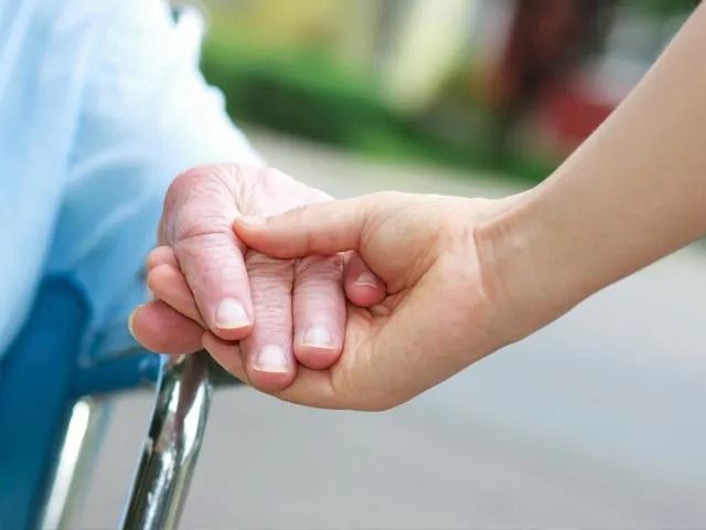 A woman is holding the hand of an elderly woman in a wheelchair.