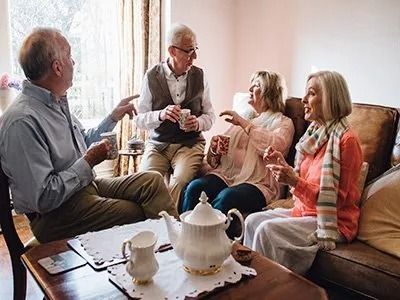 A group of elderly people are sitting around a table drinking tea.
