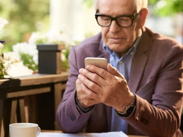 An older man is sitting at a table looking at his cell phone.