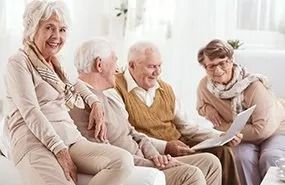 A group of elderly people are sitting on a couch looking at a book.