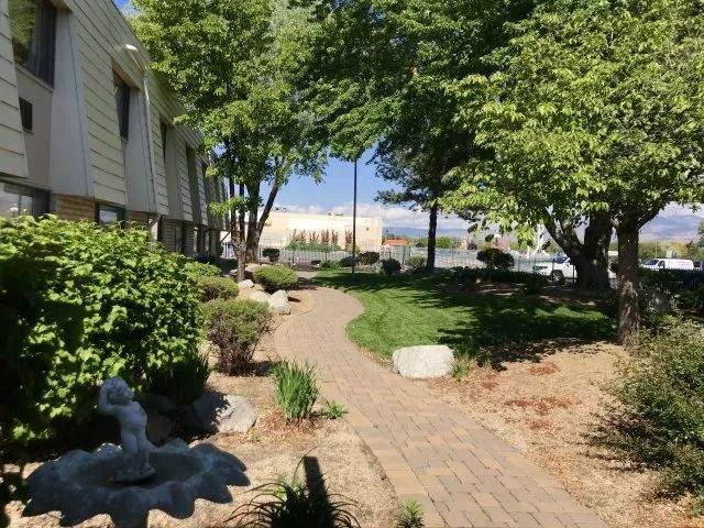 A brick walkway leading to a building with trees and bushes