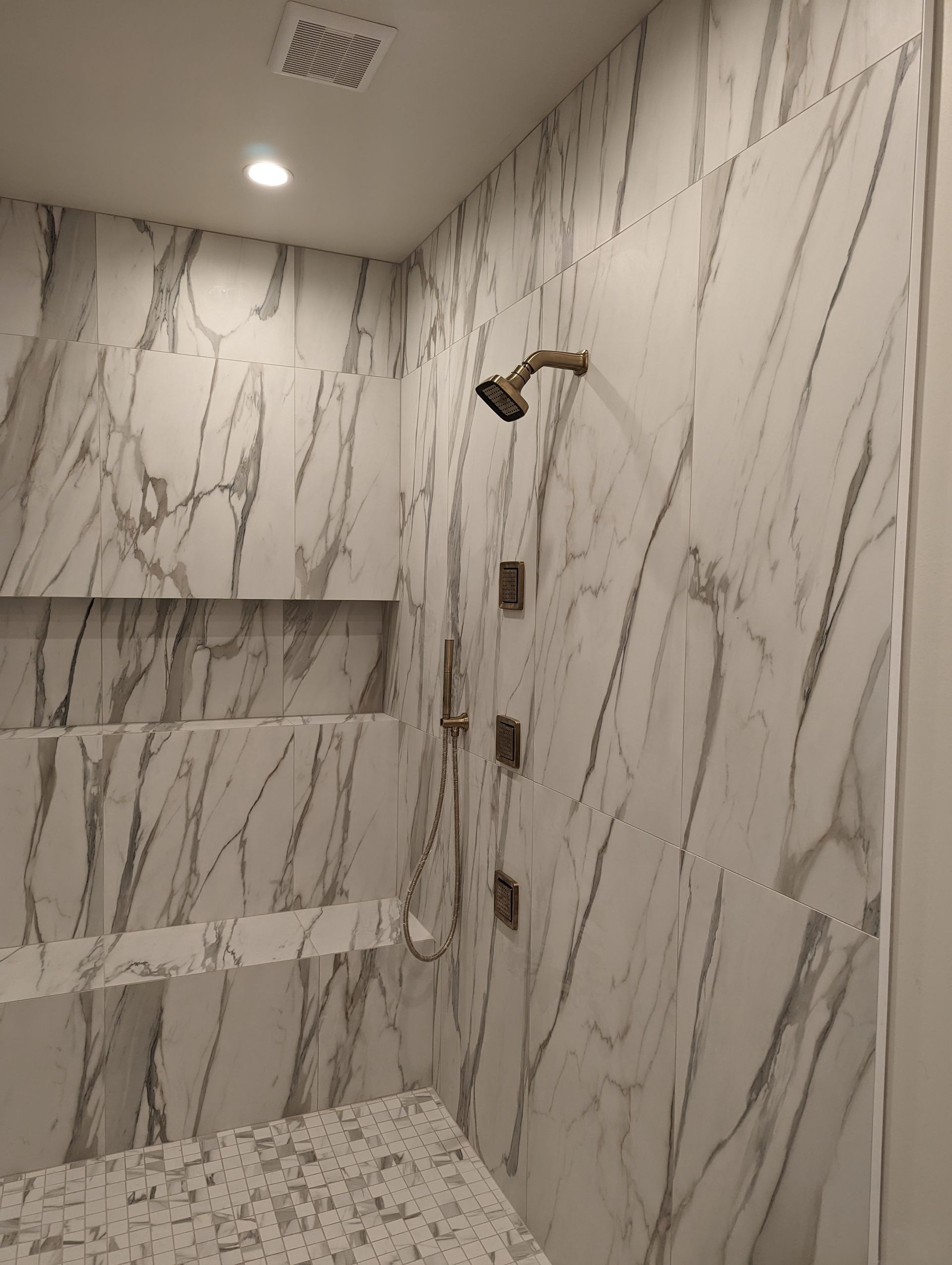 A bathroom with marble tiles and a shower head.