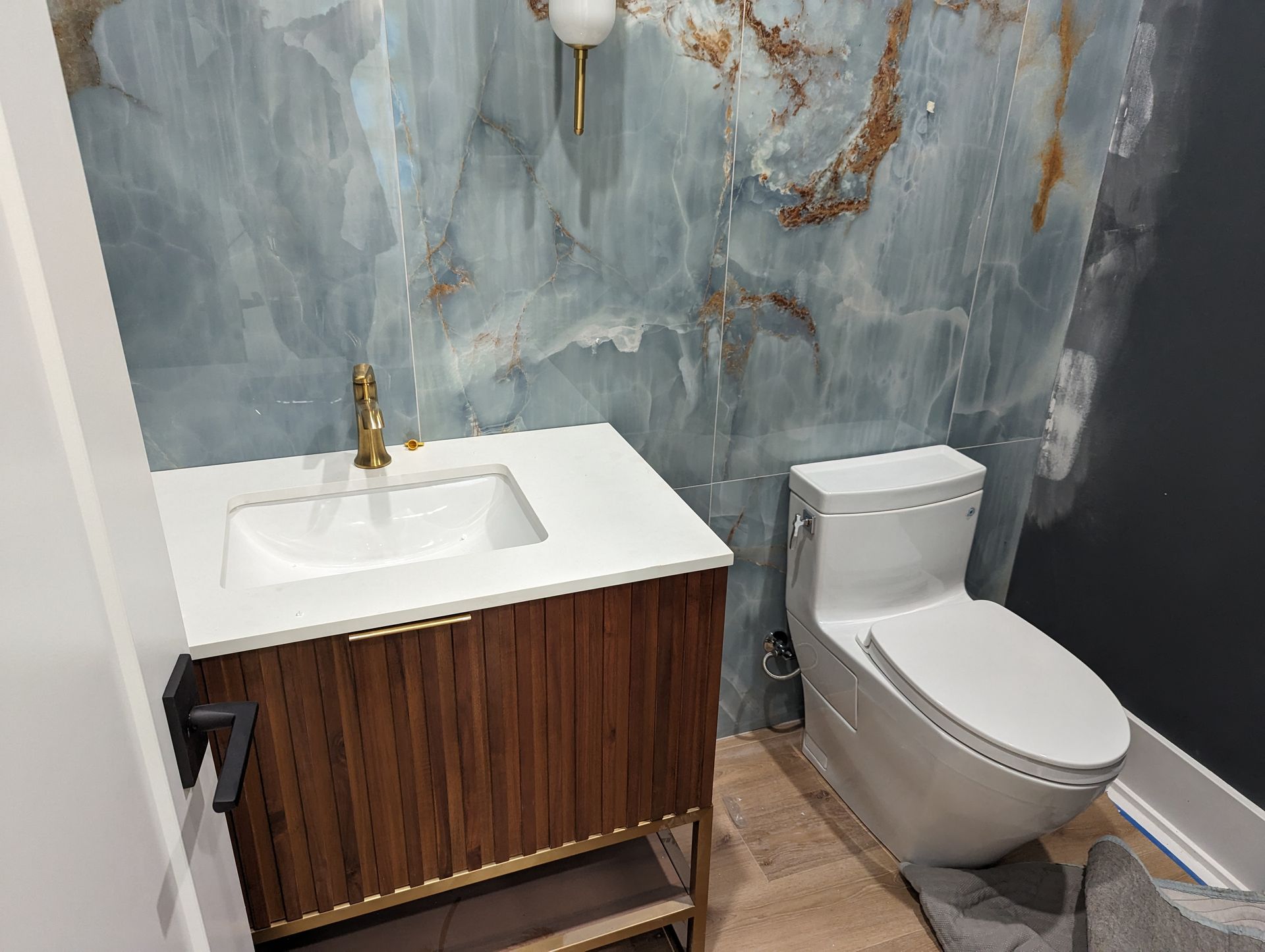 A bathroom with a toilet , sink , and marble wall.