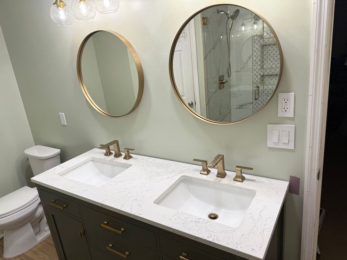 A bathroom with two sinks , a toilet , and two round mirrors.