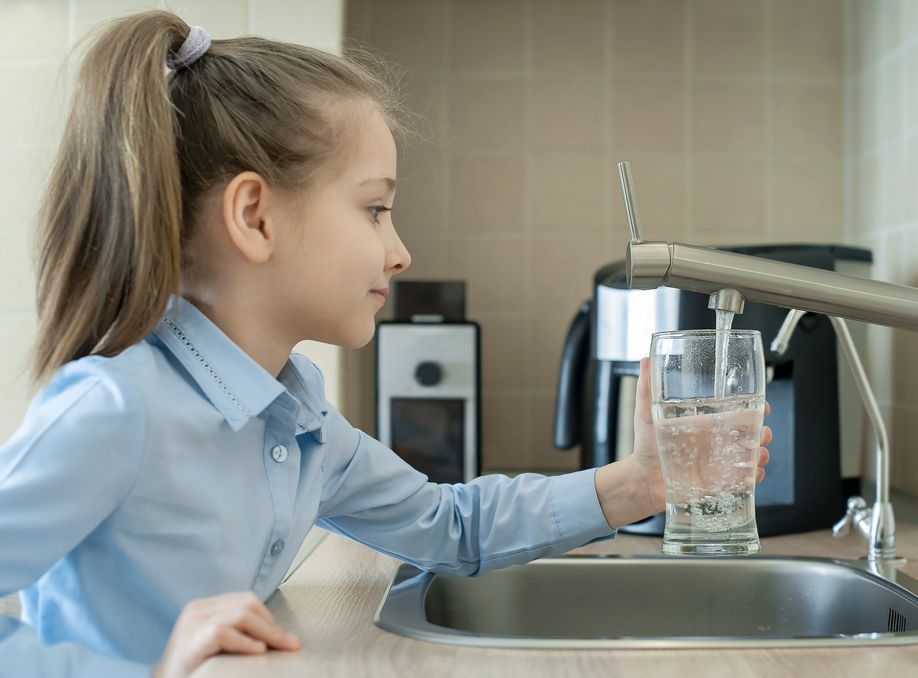 A little girl is holding a glass of water in front of a sink.