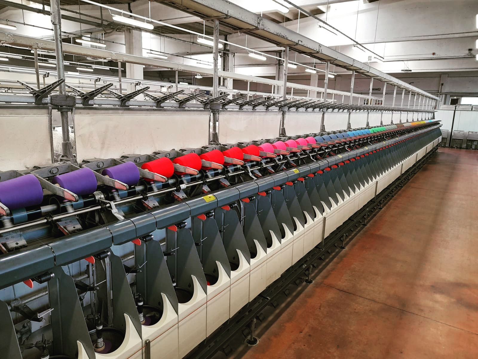 Una lunga macchina industriale per la filatura tessile all'interno di una fabbrica