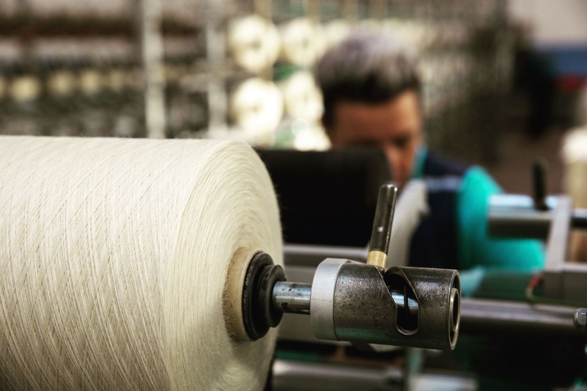 In uno stabilimento industriale, un operaio controlla una grande bobina di filato bianco su una macchina tessile.