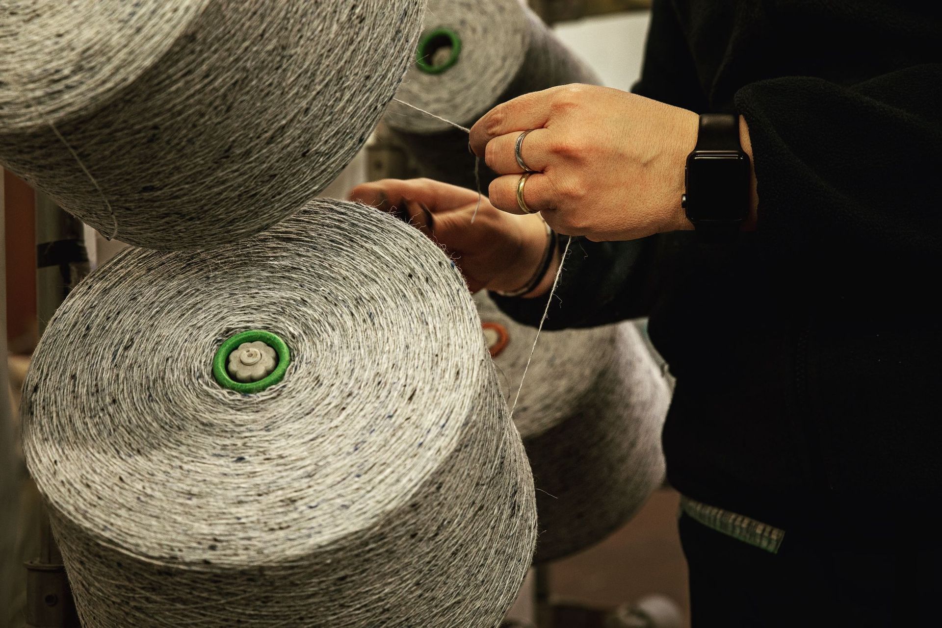 Una persona infila un filo grigio e screziato da una grande bobina su un macchinario tessile.