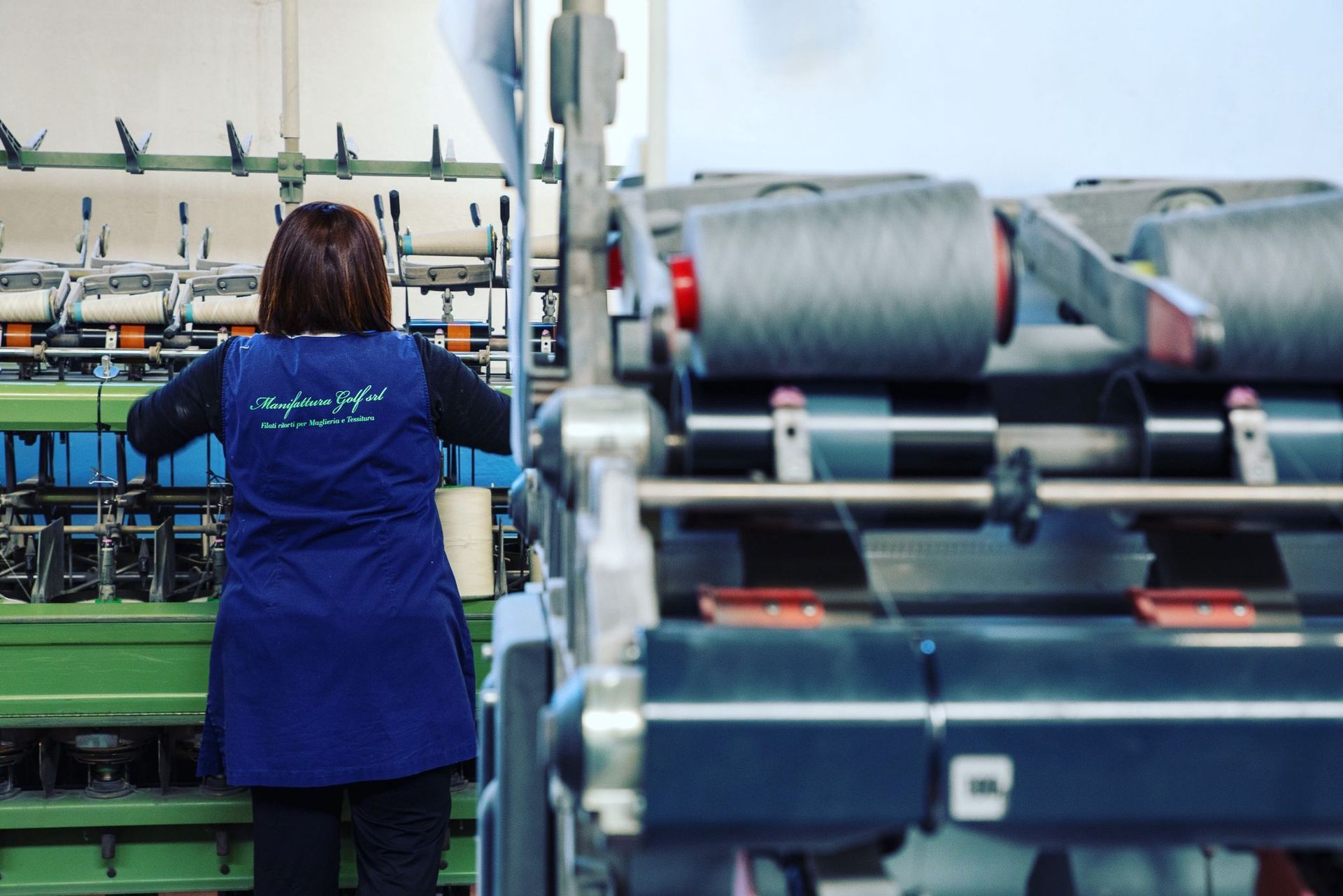 Una persona in uniforme blu al lavoro su una macchina tessile in una fabbrica.