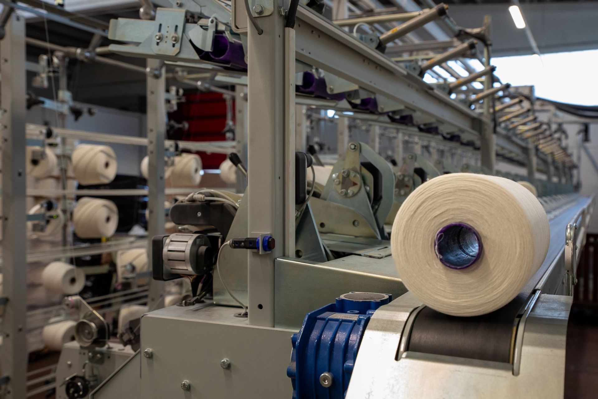 Macchinari industriali con bobine di filato bianco in un ambiente di una fabbrica tessile.