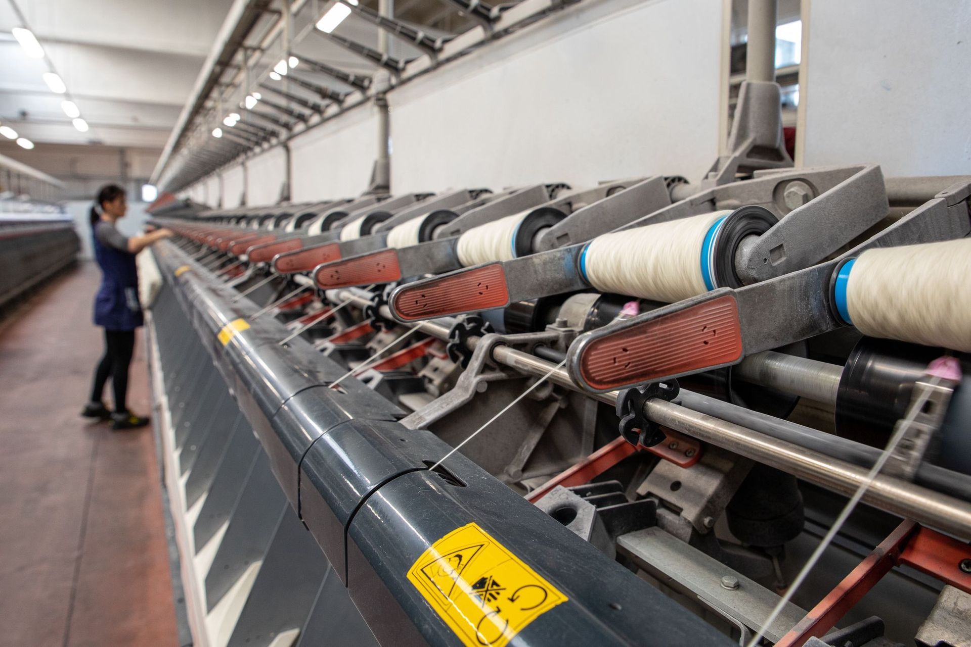 Un operaio di fabbrica aziona una lunga fila di macchine filatrici industriali con bobine di filo.