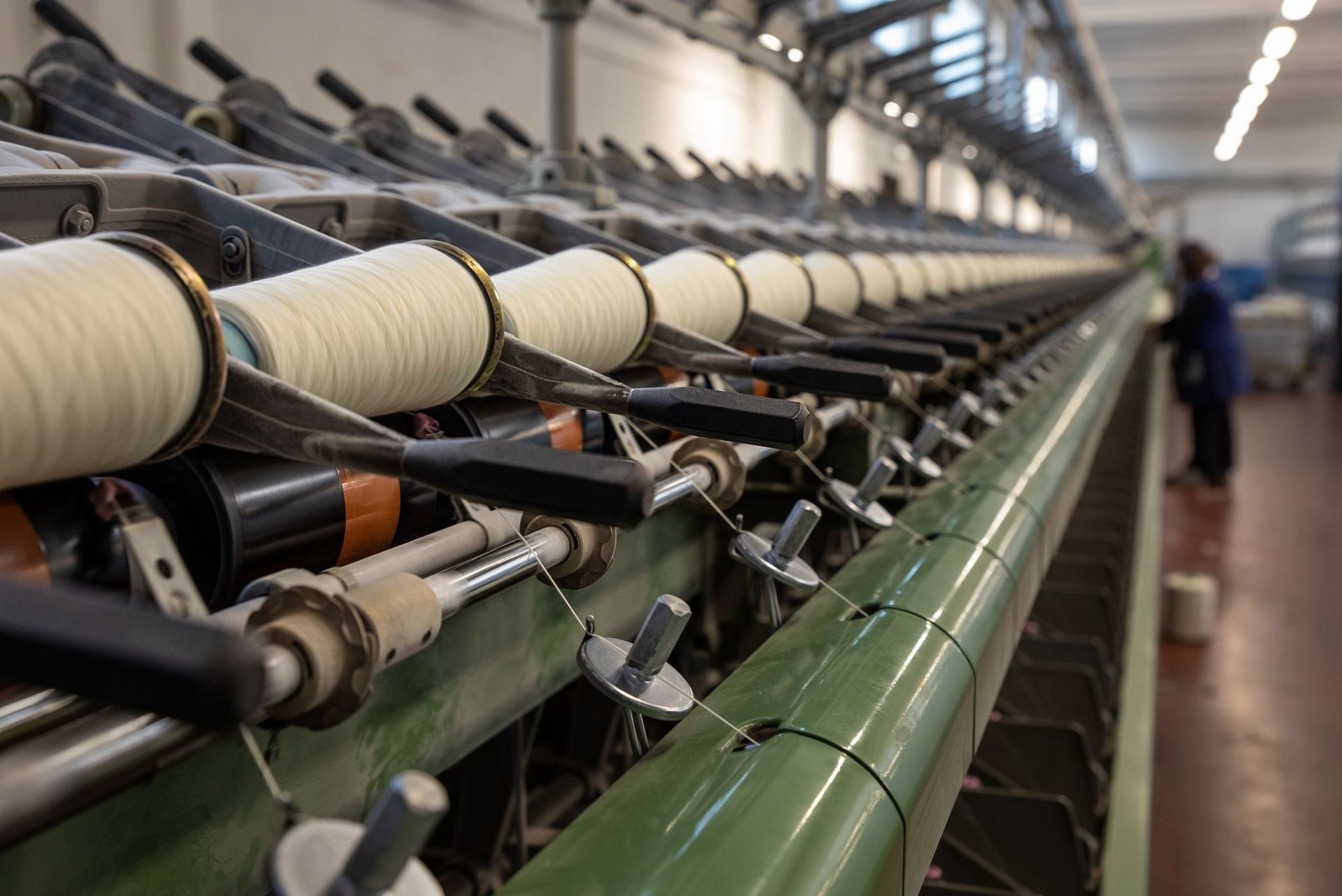 File di bobine con filo bianco su una macchina per la filatura tessile industriale in una fabbrica.
