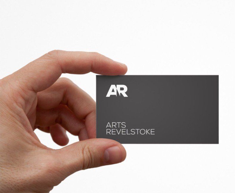 A hand is holding a business card for arts revelstoke