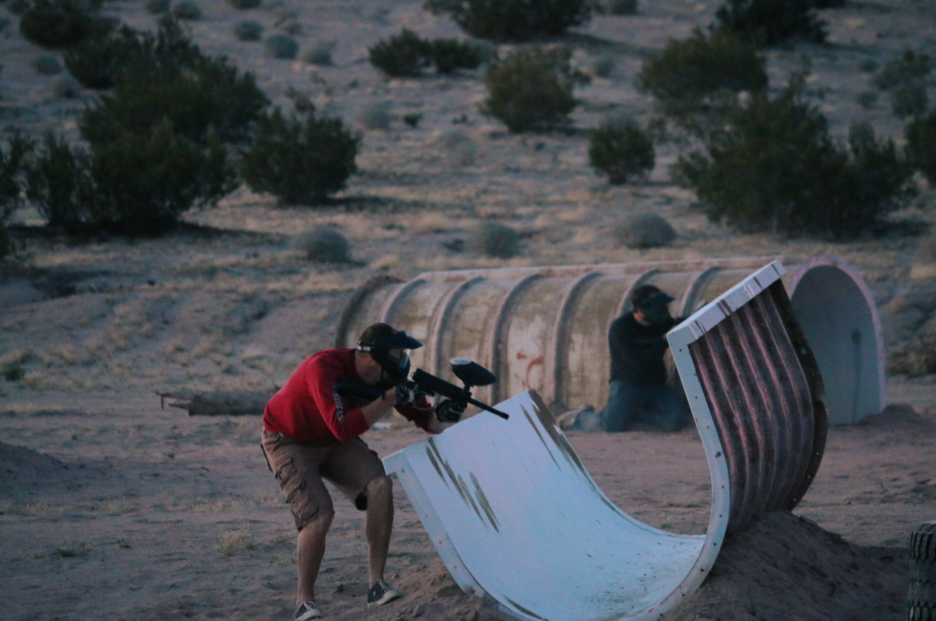 A man is playing paintball in the desert.