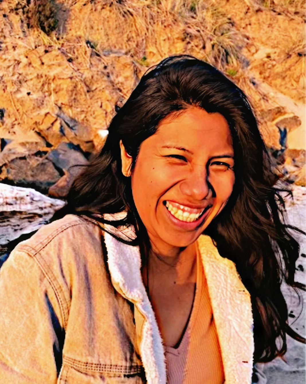 A woman with long hair is smiling and wearing a denim jacket.