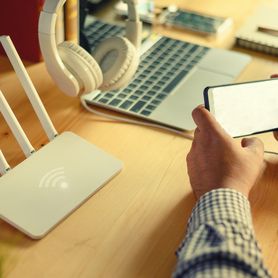 A person is holding a cell phone in front of a laptop and headphones