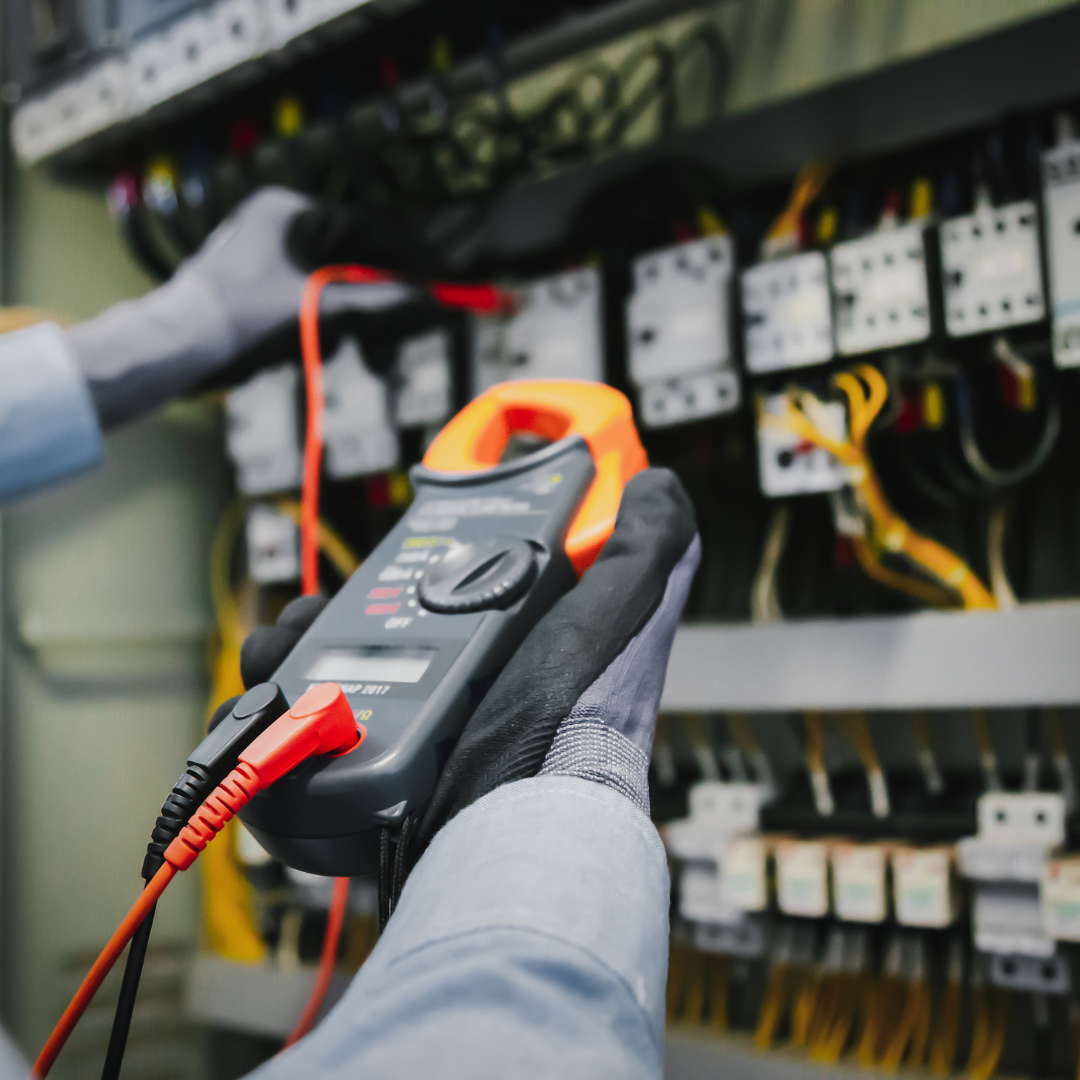 A person is holding a clamp meter in front of a electrical panel.