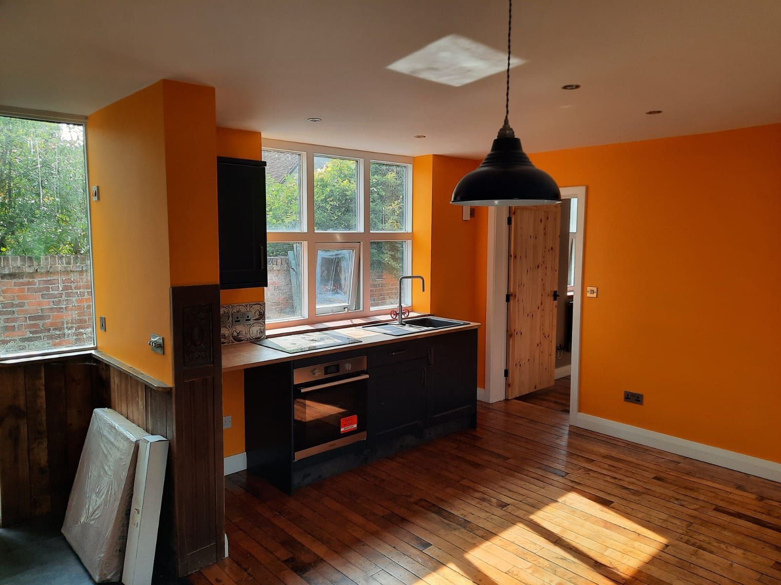 An empty kitchen with orange walls and wooden floors.