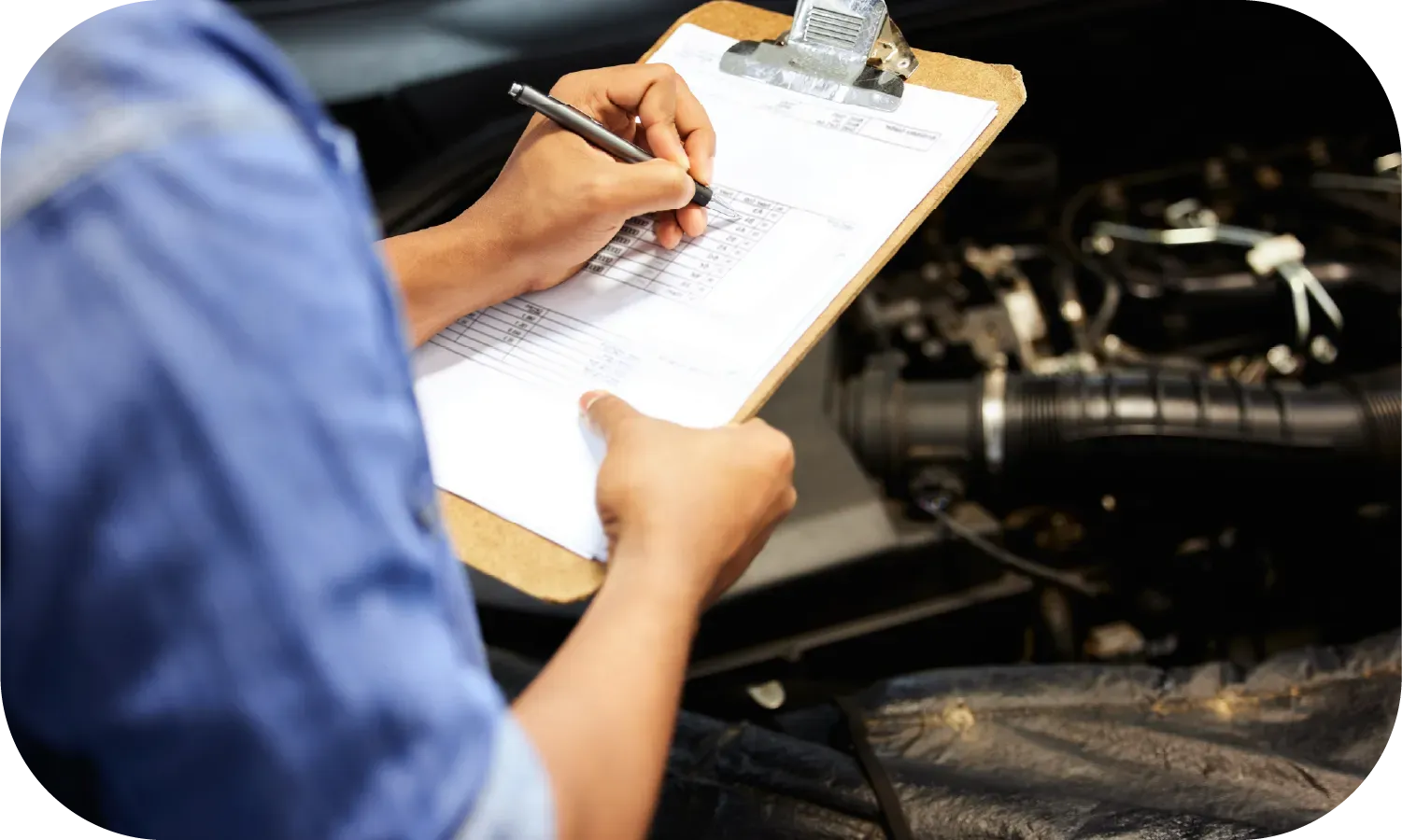 A man is writing on a clipboard in front of a car engine.