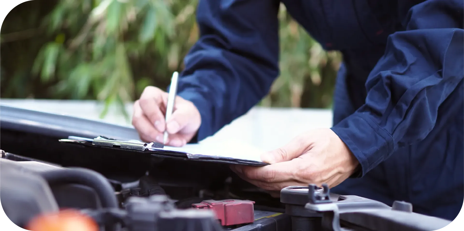 A man is writing on a clipboard while looking under the hood of a car.