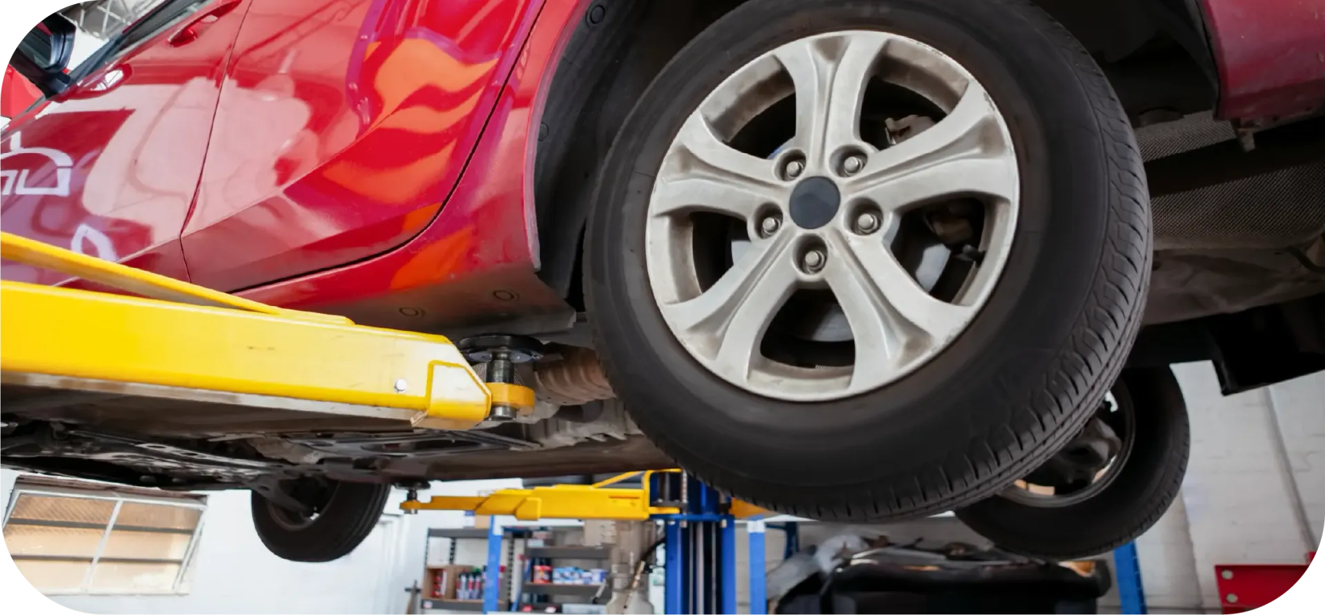 A red car is sitting on a lift in a garage.