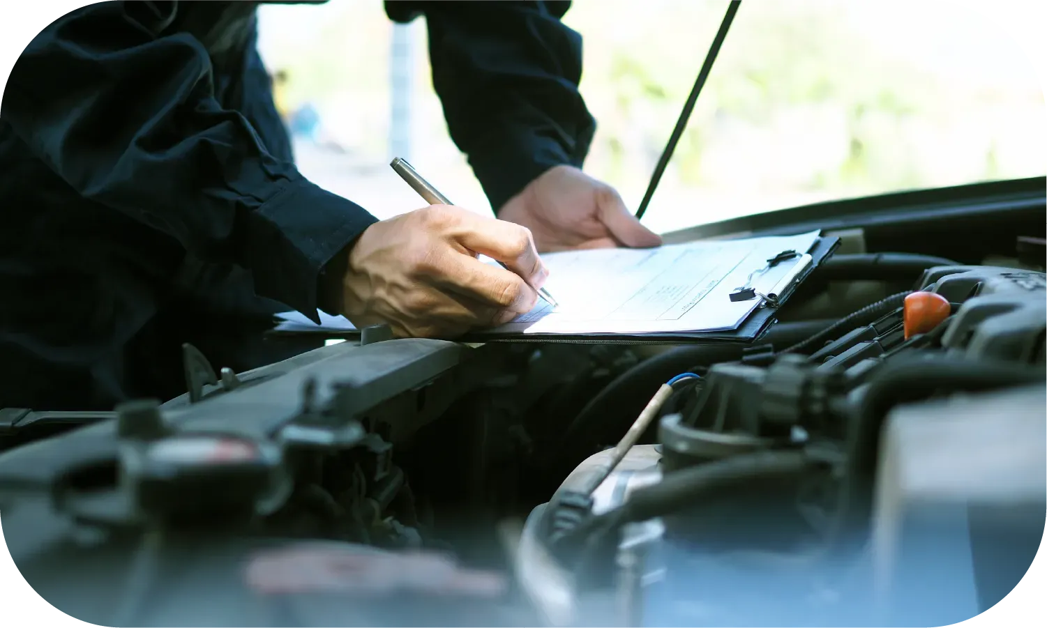 A man is writing on a clipboard while looking under the hood of a car.