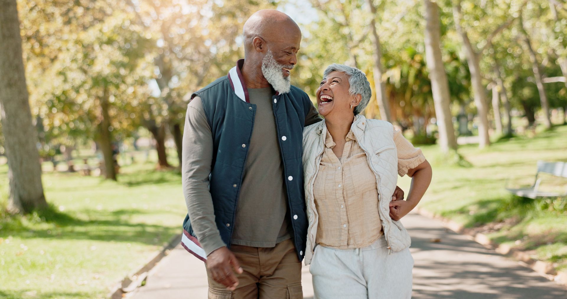 Two people smiling and walking arm in arm on a sunlit park path