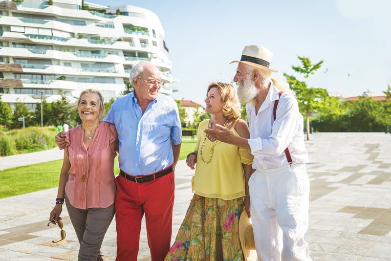 Four friends walking and chatting on a sunny resort path near a modern white building