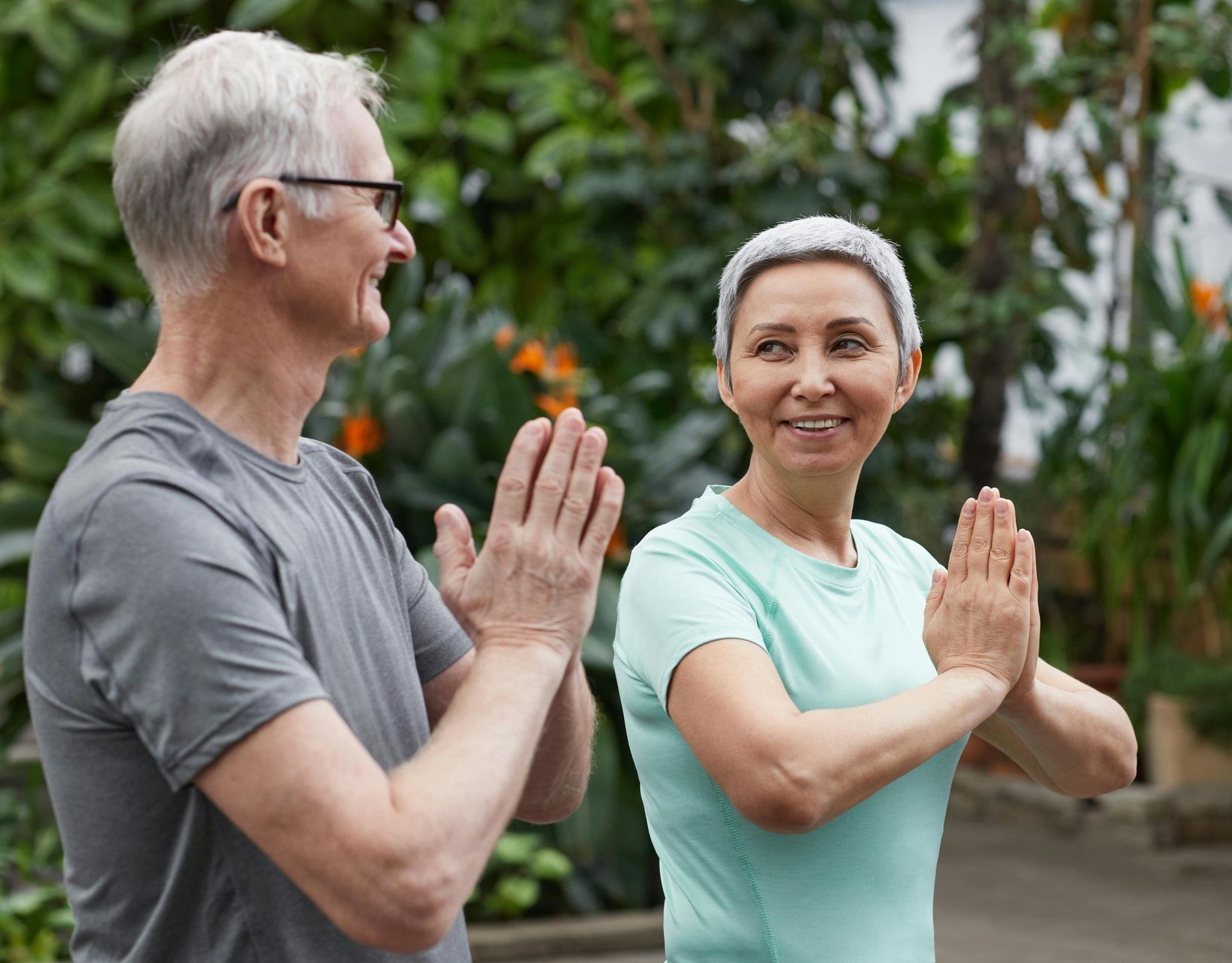Two people in athletic wear hold a yoga pose outdoors in a garden.